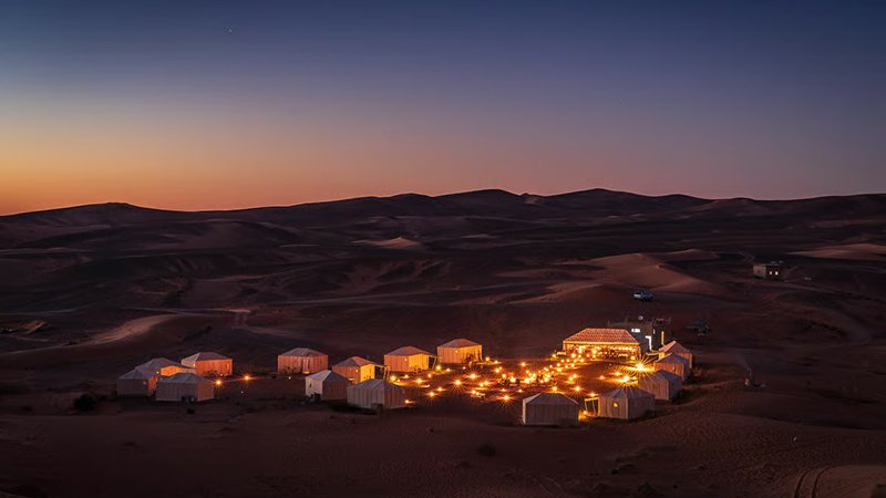 uxury tent as a golden Saharan sunrise sets the sky ablaze over endless rolling sand dunes
